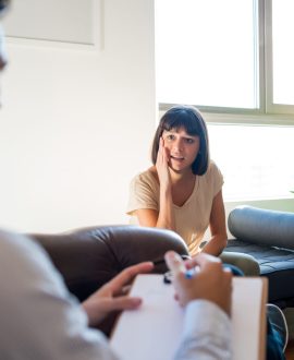 Portrait of a psychologist talking with his worried patient and taking notes during a therapy session. Psychology and mental health concept.