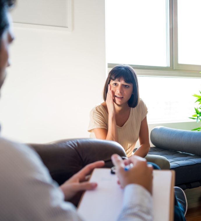 Portrait of a psychologist talking with his worried patient and taking notes during a therapy session. Psychology and mental health concept.